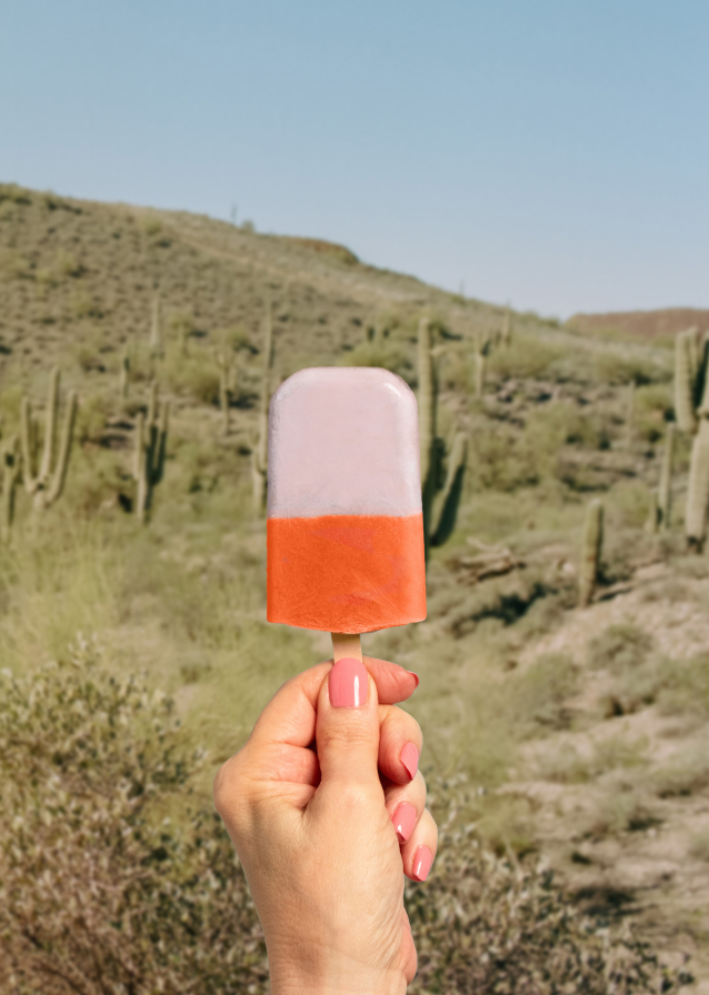 In the backdrop of Peoria AZ's rugged beauty, a hand holds a two-tone orange and white popsicle, mirroring the vibrant hues of a Saddleback sunset over cacti-dotted landscapes.