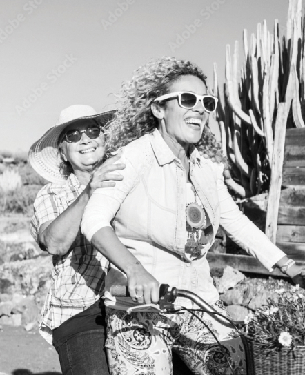 Two women, beaming with joy, ride a bicycle together through the breathtaking desert landscape of Peoria, AZ. With towering cacti in the background and the promise of Saddleback nearby, their adventure encapsulates the vibrant spirit of this enchanting locale.