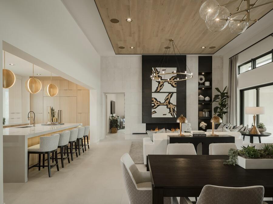 Modern open-concept living area with a kitchen, dining table, and seating. Features wood accents, abstract wall art, and a large window. Neutral color palette and contemporary lighting.