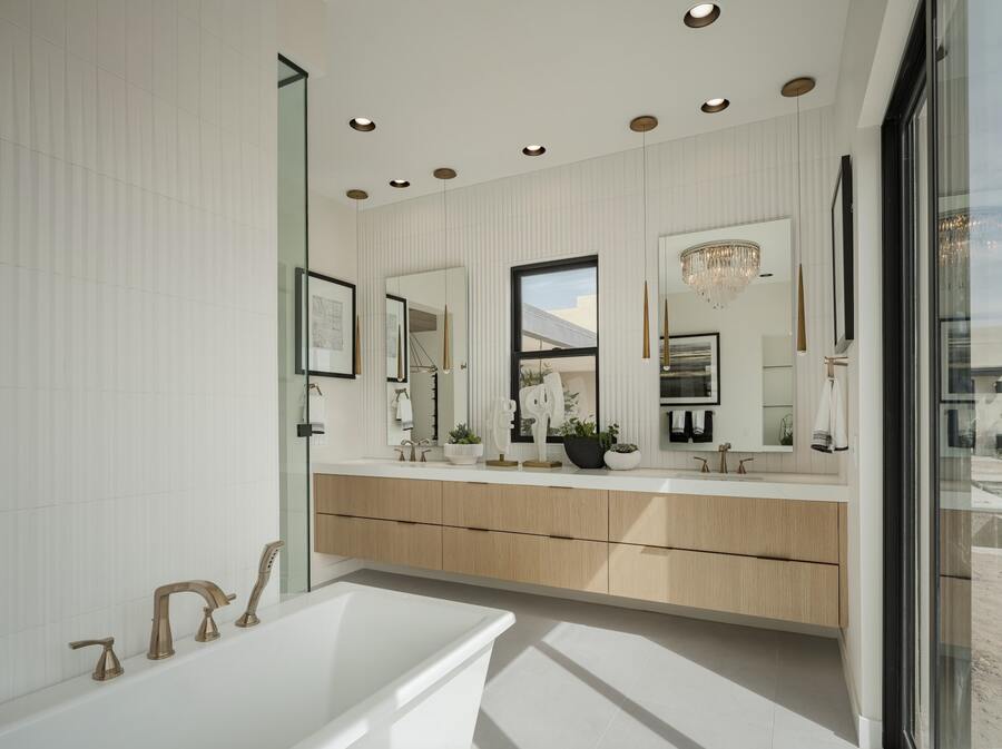 Modern bathroom with double sinks, a freestanding bathtub, and a glass-enclosed shower. Gold fixtures and circular ceiling lights add elegance. Large mirrors and windows provide ample natural light.